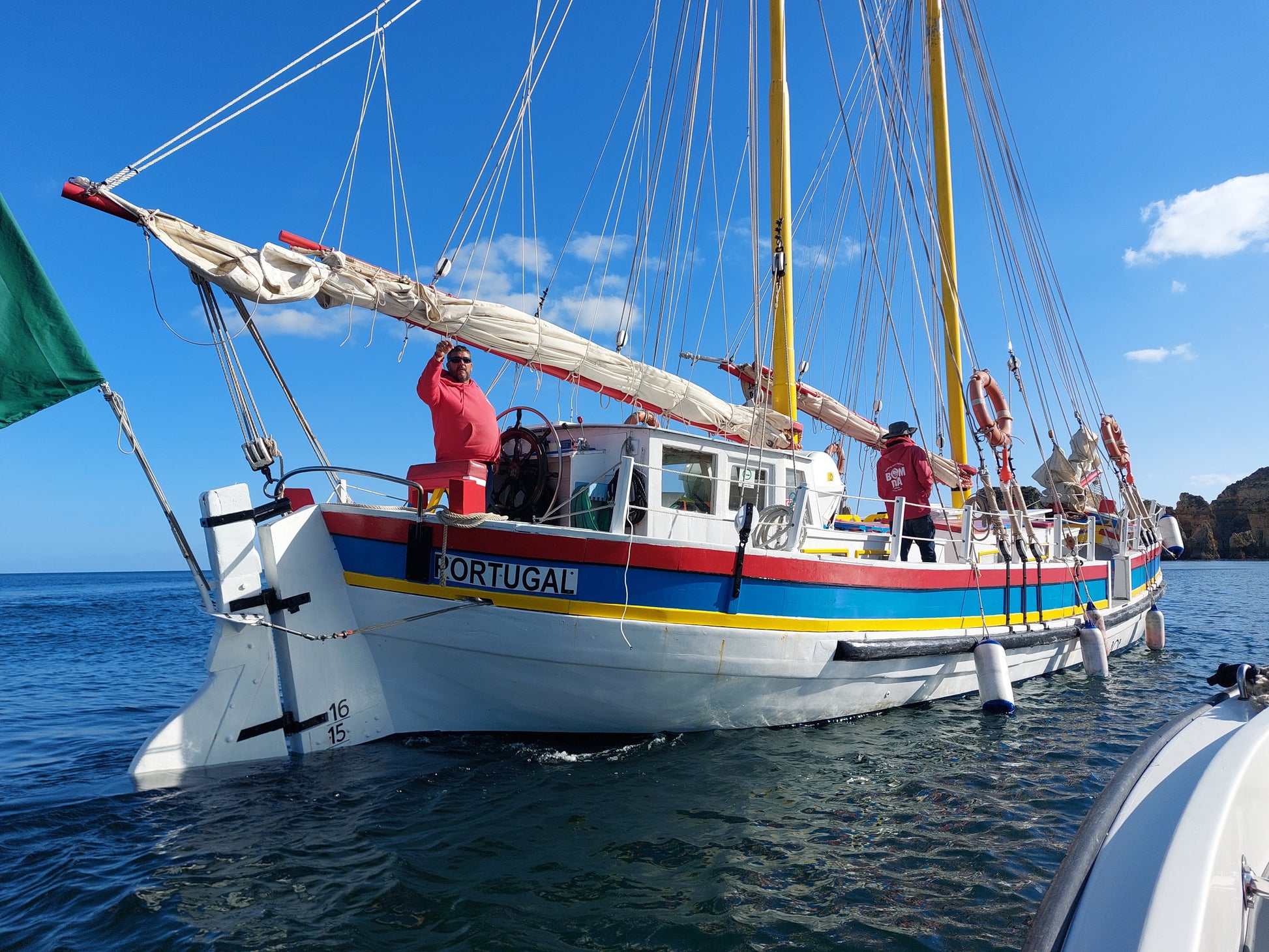 Sail boat with 'Portugal' written on it sailing on water under a blue sky off the coast of the Algarve.