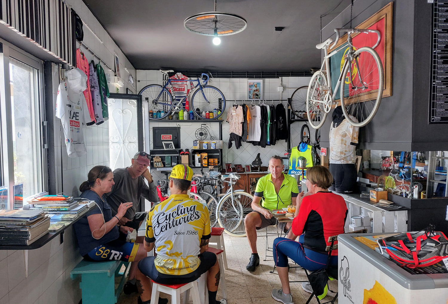 Five people, some in cycling gear, chat inside a bright café decorated with bikes and jerseys.