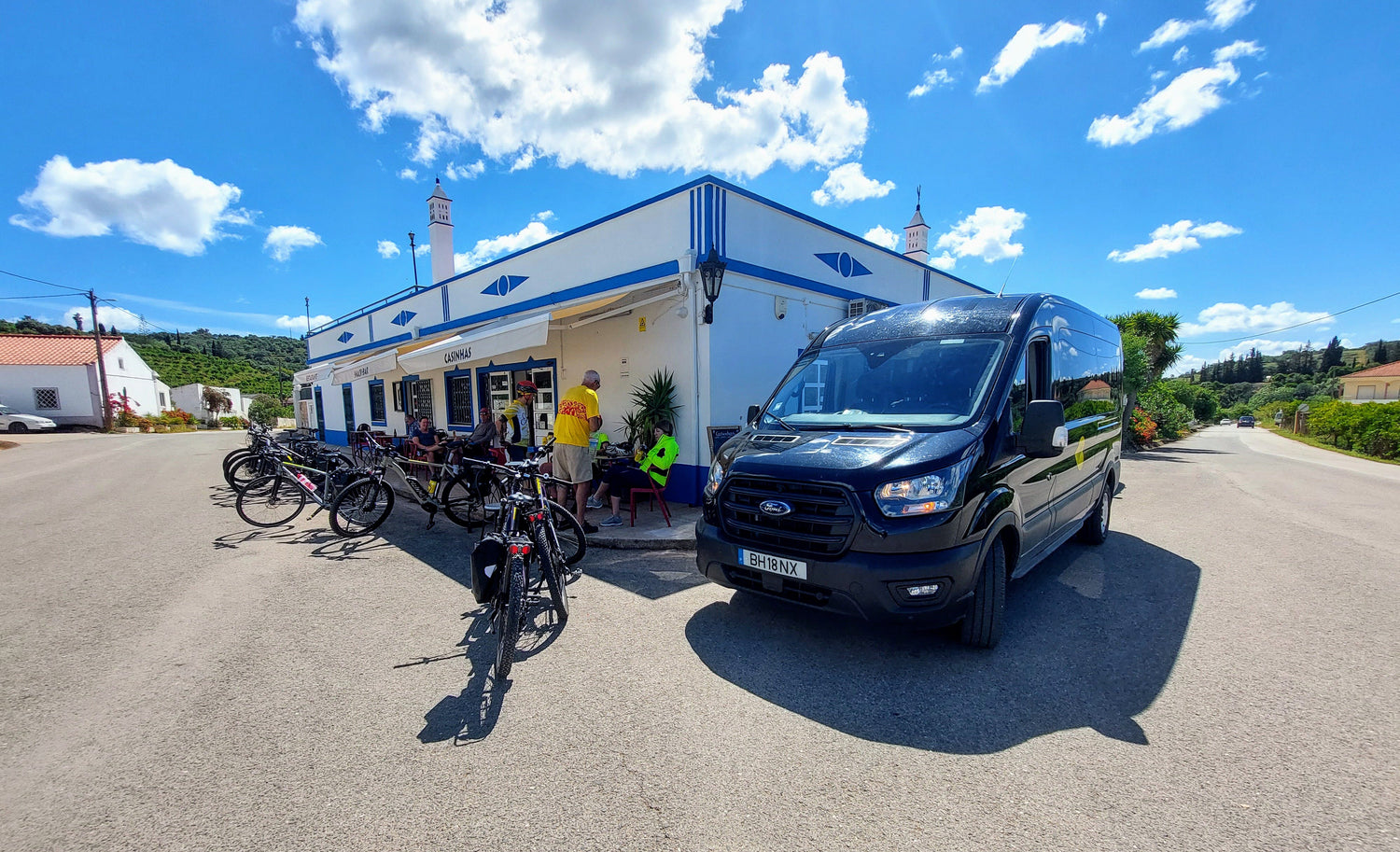 A group relaxes outside a café with blue trim during a sunny Algarve Bike Tour.