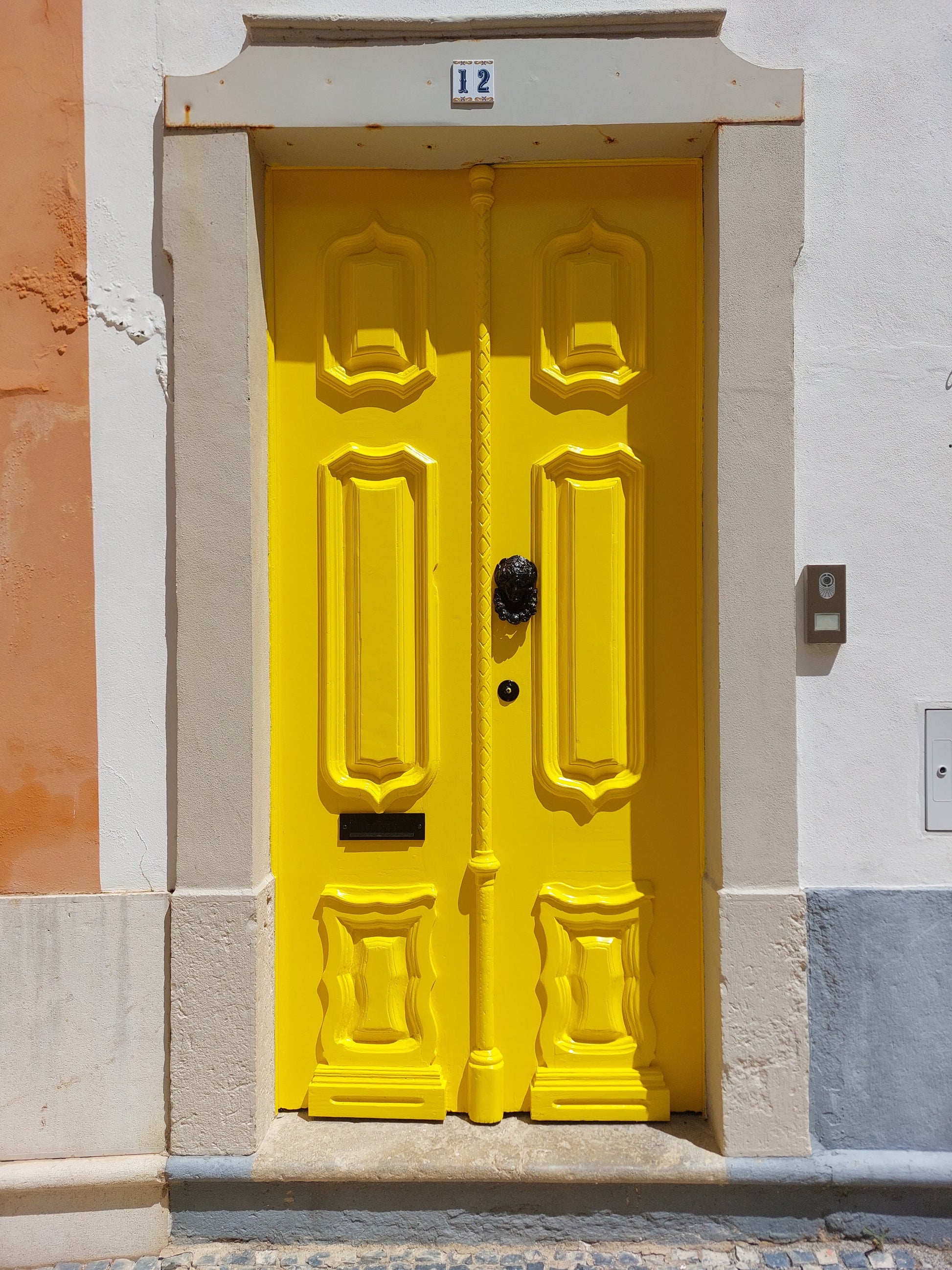 A bright yellow door with intricate detailing, framed by stonework. It's a typical Portuguese classic door.