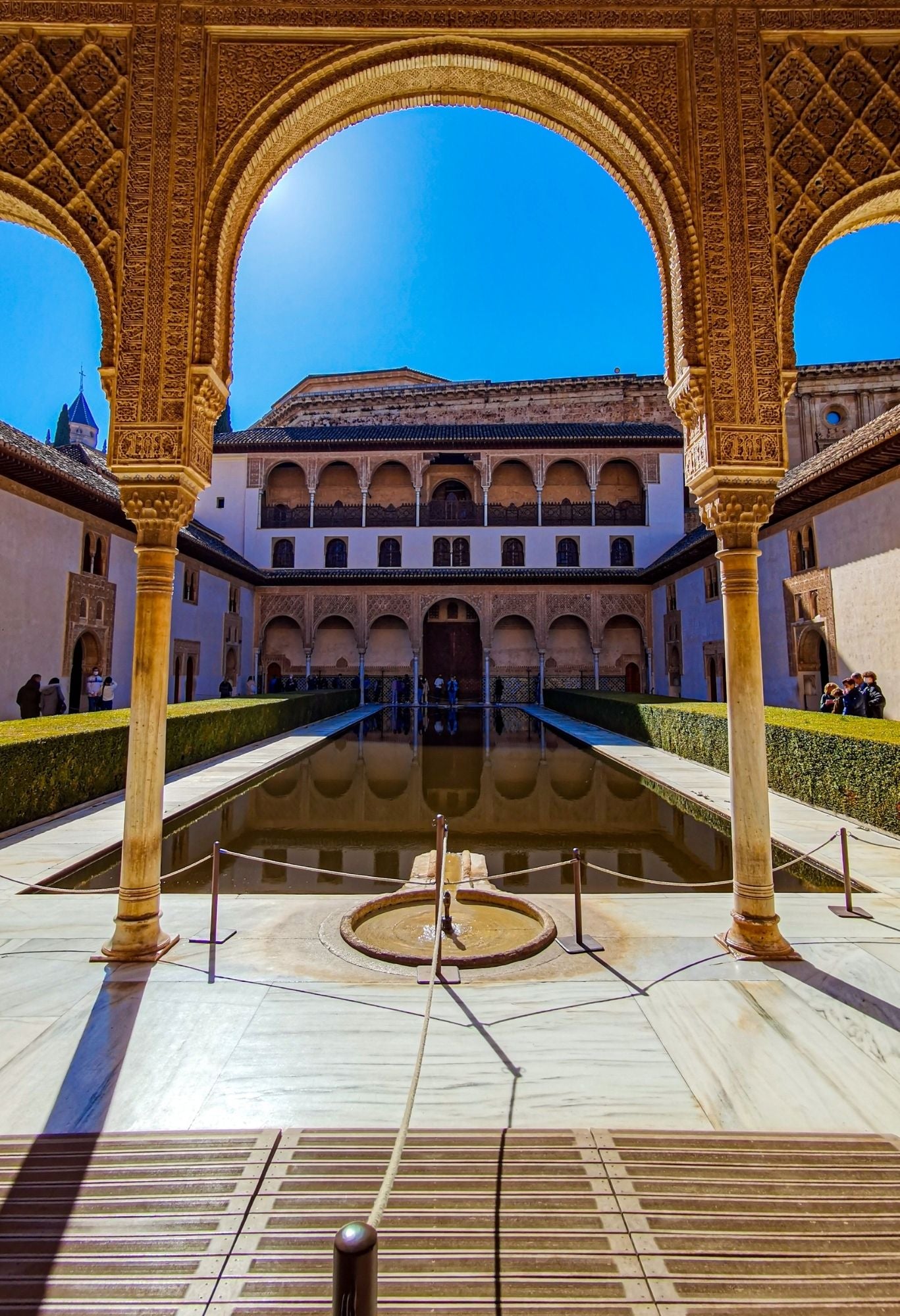 A symmetrical courtyard with arches, carvings, and a pool under blue skies on the Andalucia Bike Tour.