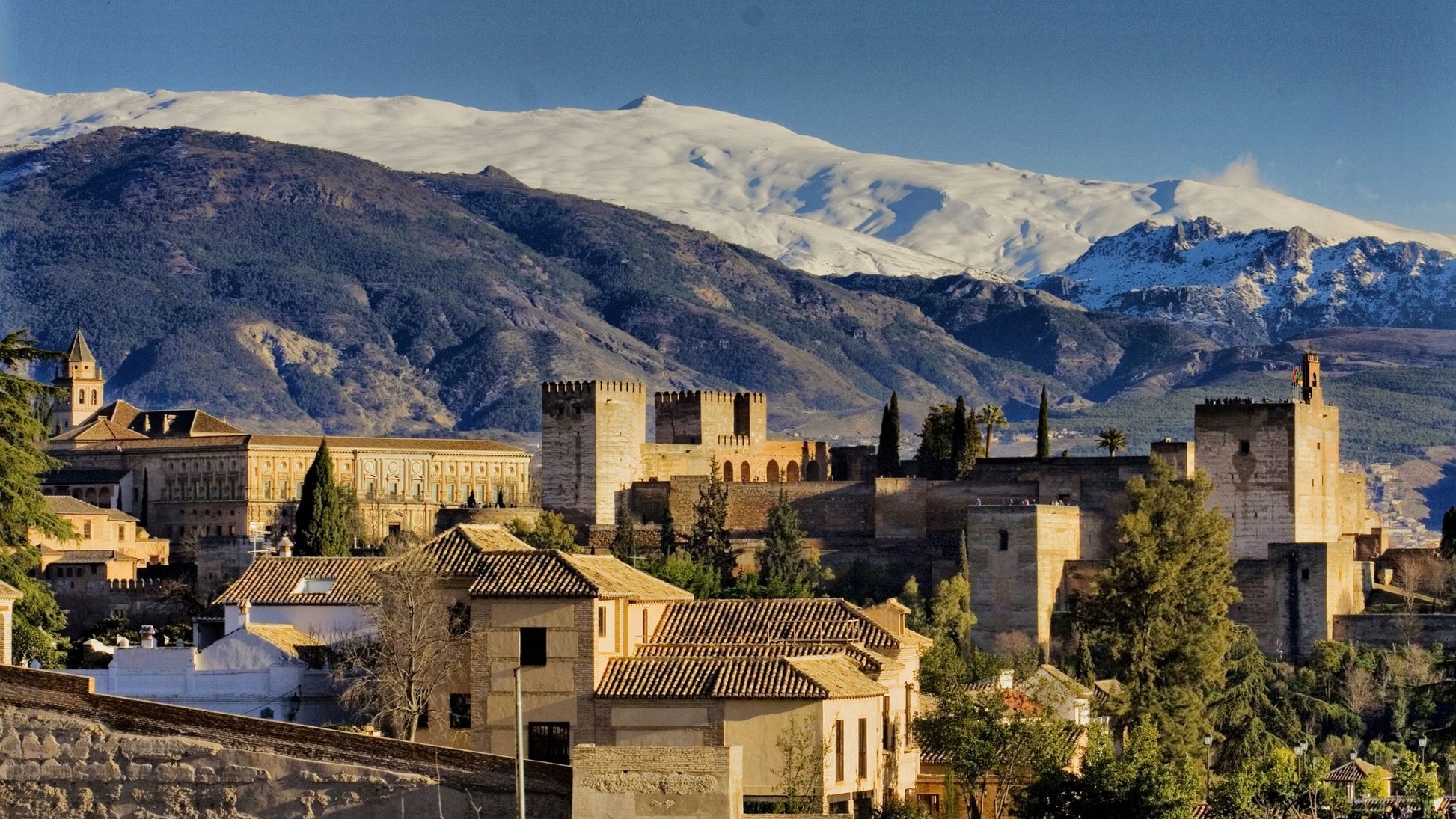 The Alhambra palace complex in Granada, Spain, with snow-capped mountains in the background under a clear sky.