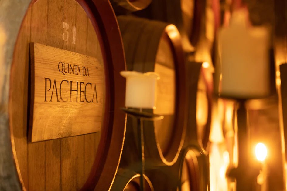 Close-up of wooden barrels labeled Quinta da Pacheca with candles in a dim cellar on the Douro Bike Tour.