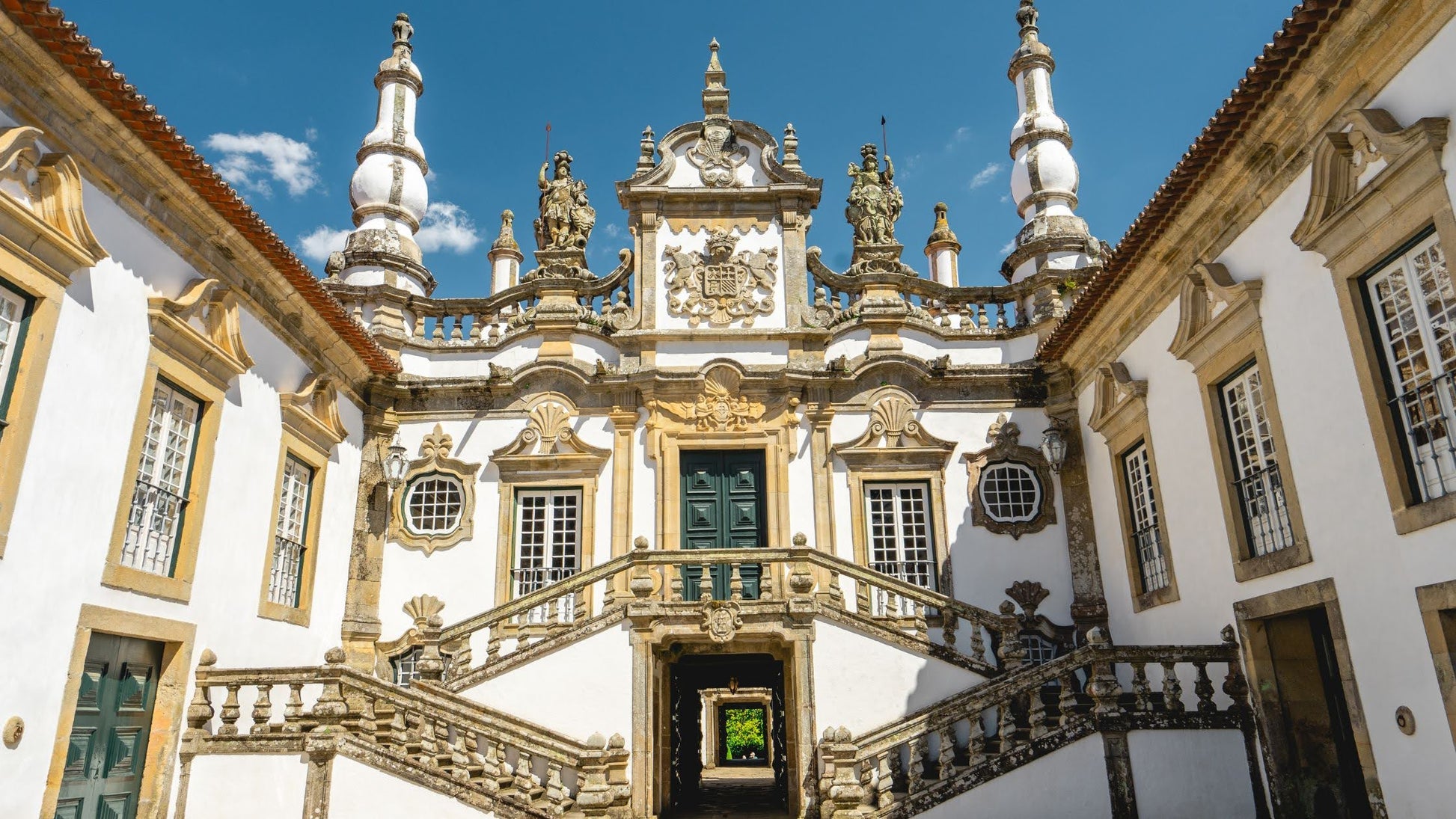Douro Bike Tour: Baroque palace with ornate façade, twin staircases, statues, and arched entry under blue sky.