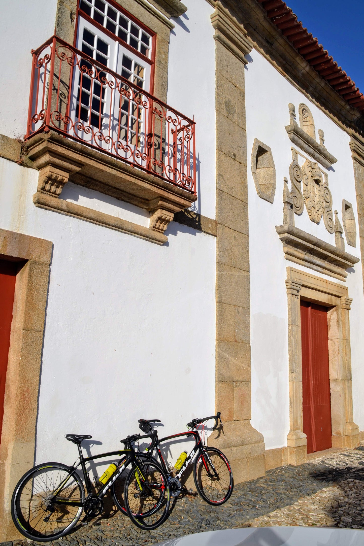 Two bikes for the Douro Bike Tour lean against a historic white stone building with red doors and a balcony.
