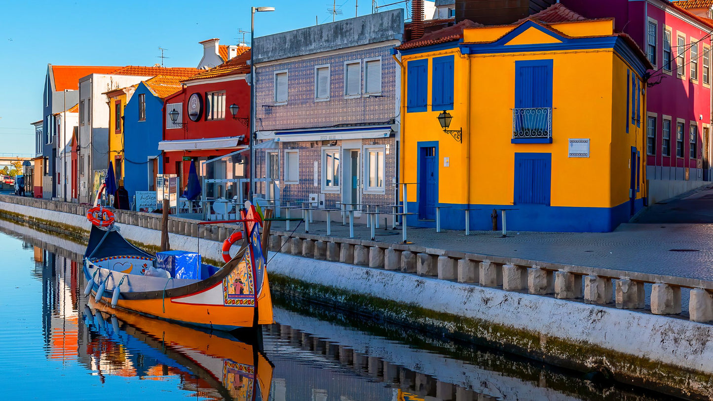 A colorful boat floats on a canal beside vibrant, multicolored houses under clear skies.