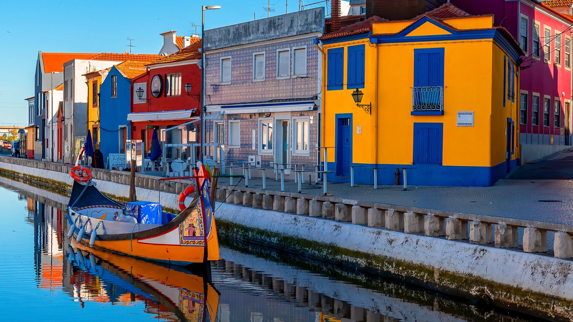 A colorful boat floats on a canal beside vibrant, multicolored houses under clear skies.