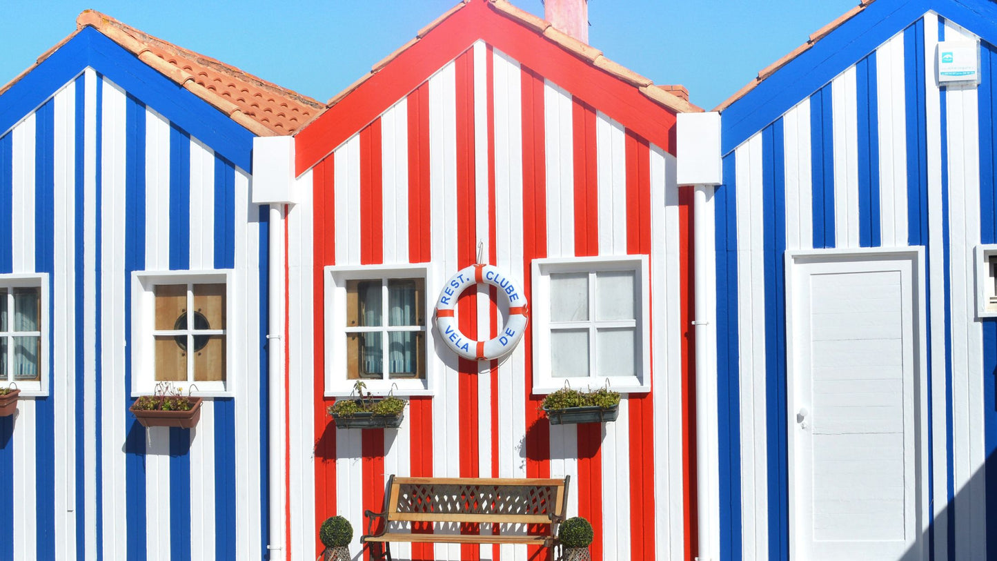 Three houses with vertical blue, red, and white stripes; central house has a lifebuoy and a wooden bench in front.