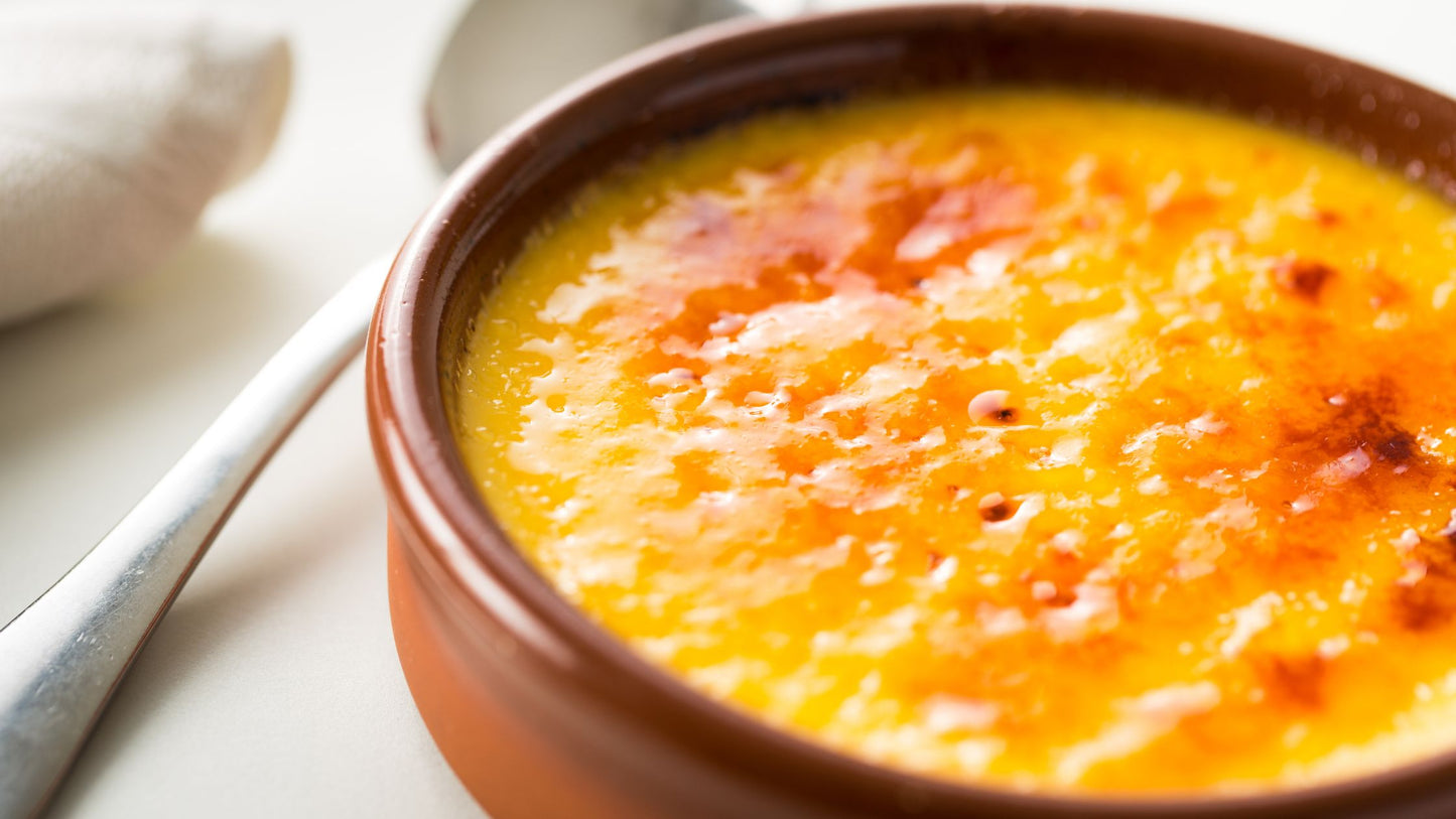 A close-up of crème brûlée in a brown ceramic dish with a golden caramelized crust.