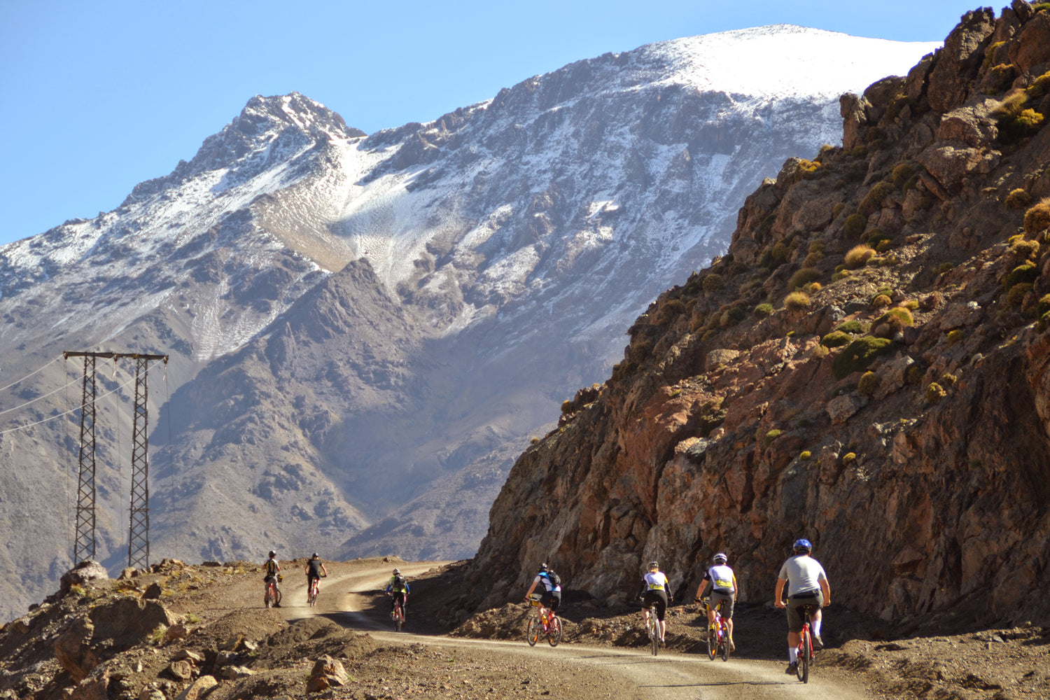 Bikers on a mountain road with snow-capped peaks in the background