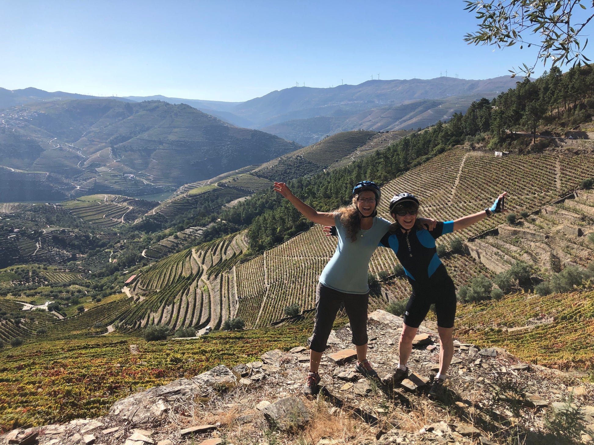 Two women standing on a rocky outcrop in the Douro valley, with vineyards and mountains in the background