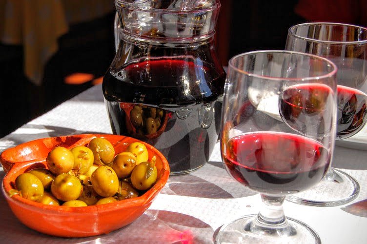 Table setting with a bowl of olives, a carafe, and two glasses of red wine.